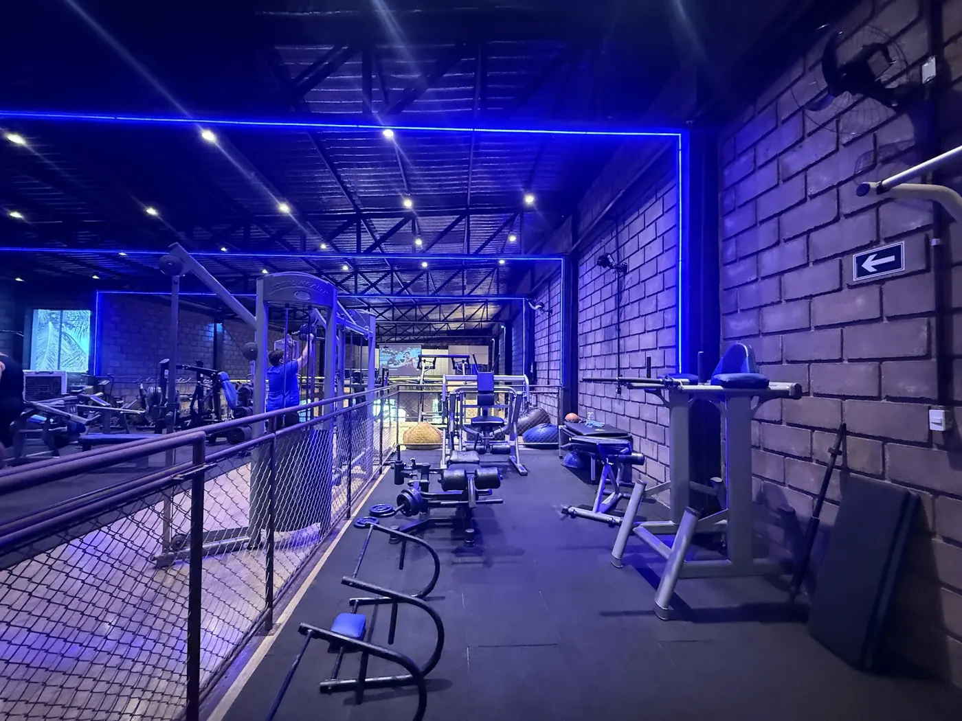 Andar de cima com aparelhos de musculação e faixa de LED azul no teto