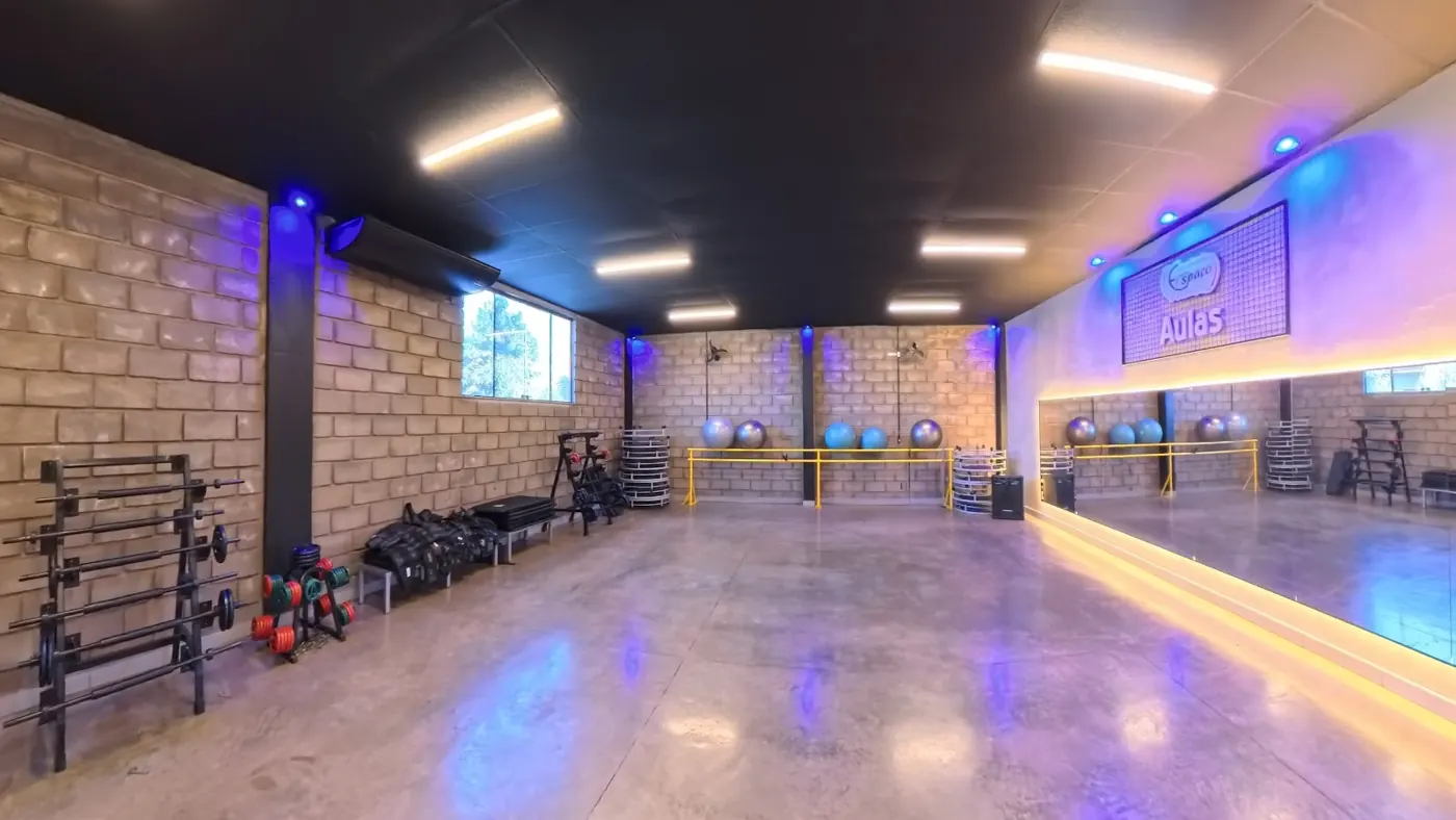 Sala de aulas coletivas com espelho, piso claro, parede de tijolinho e luz de LED azul