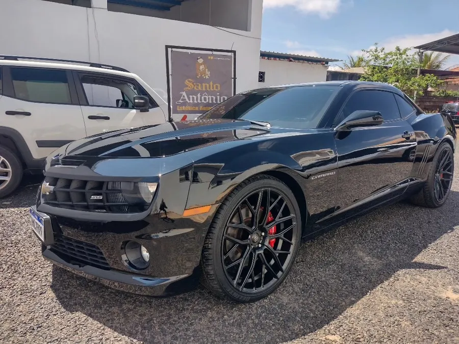 Chevrolet Camaro preto, limpo e brilhando, no pátio da loja, com a faixa da Santo Antônio ao fundo